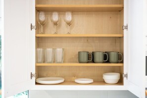 A kitchen cabinet with shelves containing wine glasses, glassware, and plates.