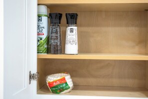 A kitchen pantry with shelves holding olive oil, black peppercorn, and sea salt.