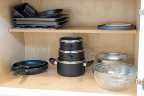 A kitchen with a wooden shelf holding cookware, including a frying pan, a pot, and a strainer.