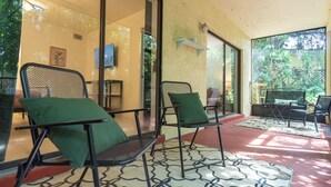 Une pièce baignée de lumière, avec une porte vitrée donnant sur un jardin, et meublée de chaises en métal et d’une petite table.