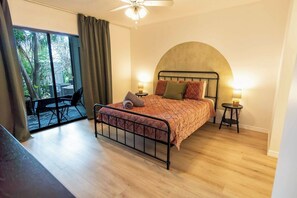 Un dormitorio con cama, dos mesitas de noche, un ventilador de techo y vistas al exterior.