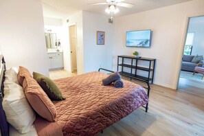 Une chambre à coucher comprenant un lit, une télévision, un bureau et donnant sur un espace de vie.
