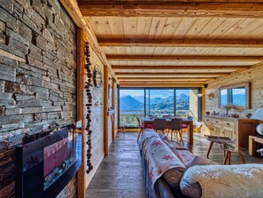 Een gezellig interieur van een chalet met een stenen muur, een open haard, een eethoek en uitzicht op bergen.
