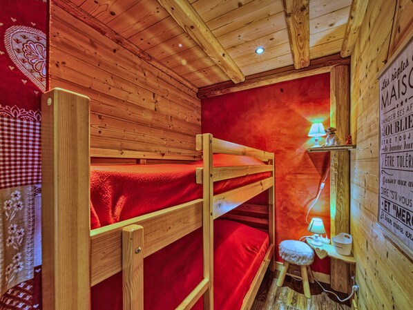 Een knus houten vertrek met stapelbedden en een klein nachtkastje met een lamp.