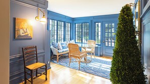 Una habitación con pared azul, suelo de madera, muebles de mimbre y un ventanal grande.