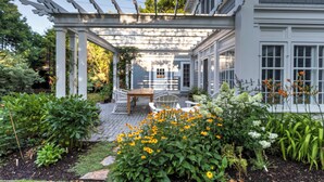 Un patio cubierto con una mesa y sillas, rodeado de un jardín con diversas plantas y flores.