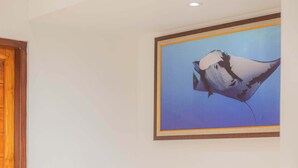 Ein beiges Sofa mit zwei Kissen vor einer weißen Wand, darüber ein gerahmtes Bild eines Vogels und eine Holztür links.