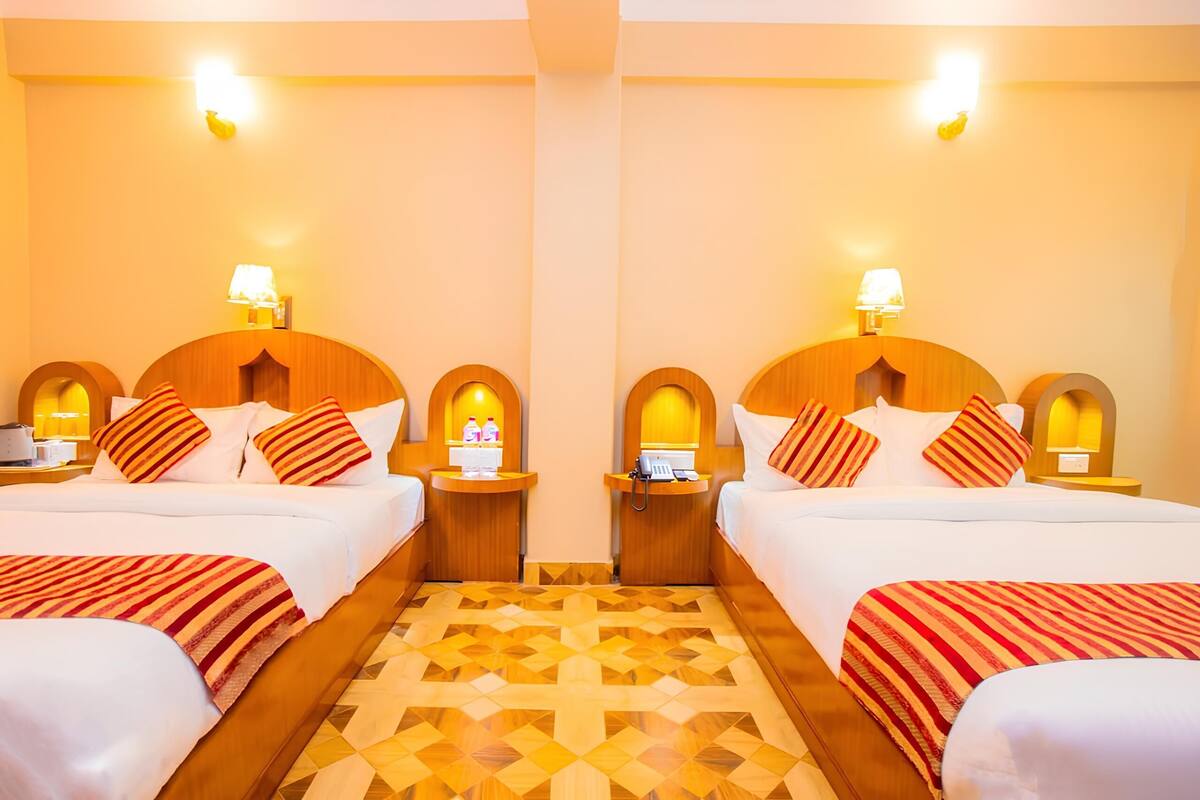 A mirrored hotel room with two beds, wooden headboards, bedside tables with lamps, and a patterned floor.