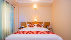 A hotel room with a large bed, a bedside table with a lamp, a phone, and a small table with a bottle and a glass. - Hotel Liberty (Pokhara)