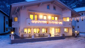 Un hôtel de deux étages doté d’un balcon décoré de guirlandes lumineuses, d’une enseigne indiquant « LA VITA » et offrant une vue sur des montagnes enneigées.