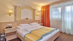 Une chambre d’hôtel avec un grand lit, deux tables de chevet, une commode, un miroir et une fenêtre avec des rideaux légers.