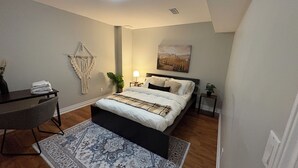 A bedroom with a bed, a desk, a chair, a macrame wall hanging, a lamp, and a painting on the wall. - Beautiful Priv. bsmt 2B 1Bath apartment w/ parking (Brampton)