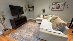 A living room with a flat-screen TV, a beige sofa, patterned rugs, and decorative wall shelves. - Beautiful Priv. bsmt 2B 1Bath apartment w/ parking (Brampton)