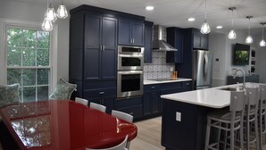 Una cocina moderna con gabinetes azul oscuro, electrodomésticos de acero inoxidable y una mesa de comedor roja.
