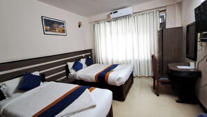 A hotel room with two beds, a desk, a chair, a TV, and a window with curtains. - Karma Traveller's Home (Kathmandu)