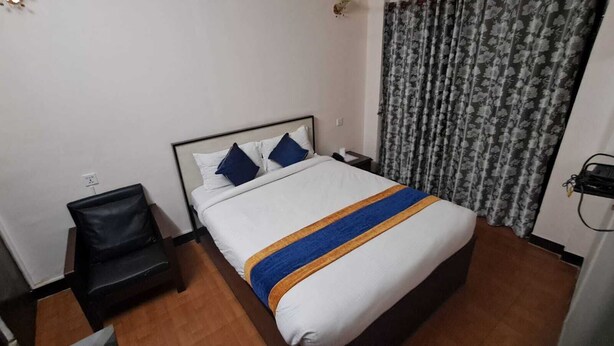 A hotel room with a bed, a chair, a nightstand, and a curtain. - Karma Traveller's Home (Kathmandu)