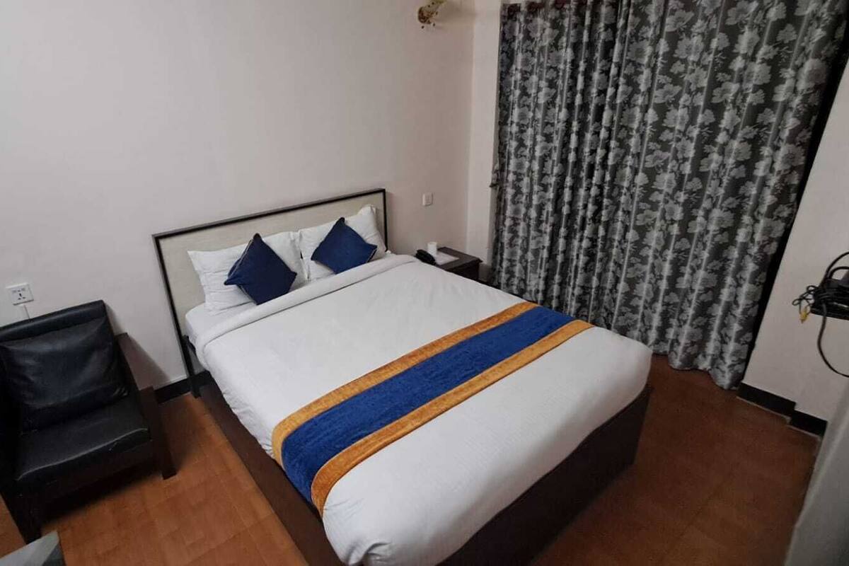 A hotel room with a bed, a chair, a nightstand, and a curtain.