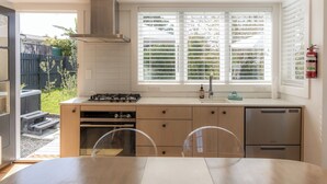 Une cuisine moderne équipée d’une cuisinière à gaz, d’un four et d’un lave-vaisselle, avec une fenêtre dotée de stores et donnant sur le jardin arrière.