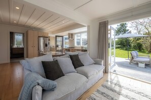 A modern living room with a light-colored sofa, a dining area, and a kitchen. - Tahatai Cottage with Spa Pool - Oneroa (Waiheke Island)