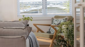 Un coin salon confortable avec un fauteuil moelleux et un canapé, une plante en pot et une fenêtre avec des stores.