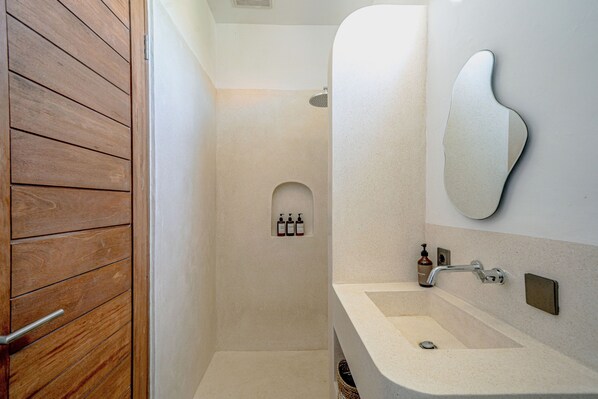 Un bagno con porta in legno, una doccia, un lavabo con specchio e articoli da toilette a parete.
