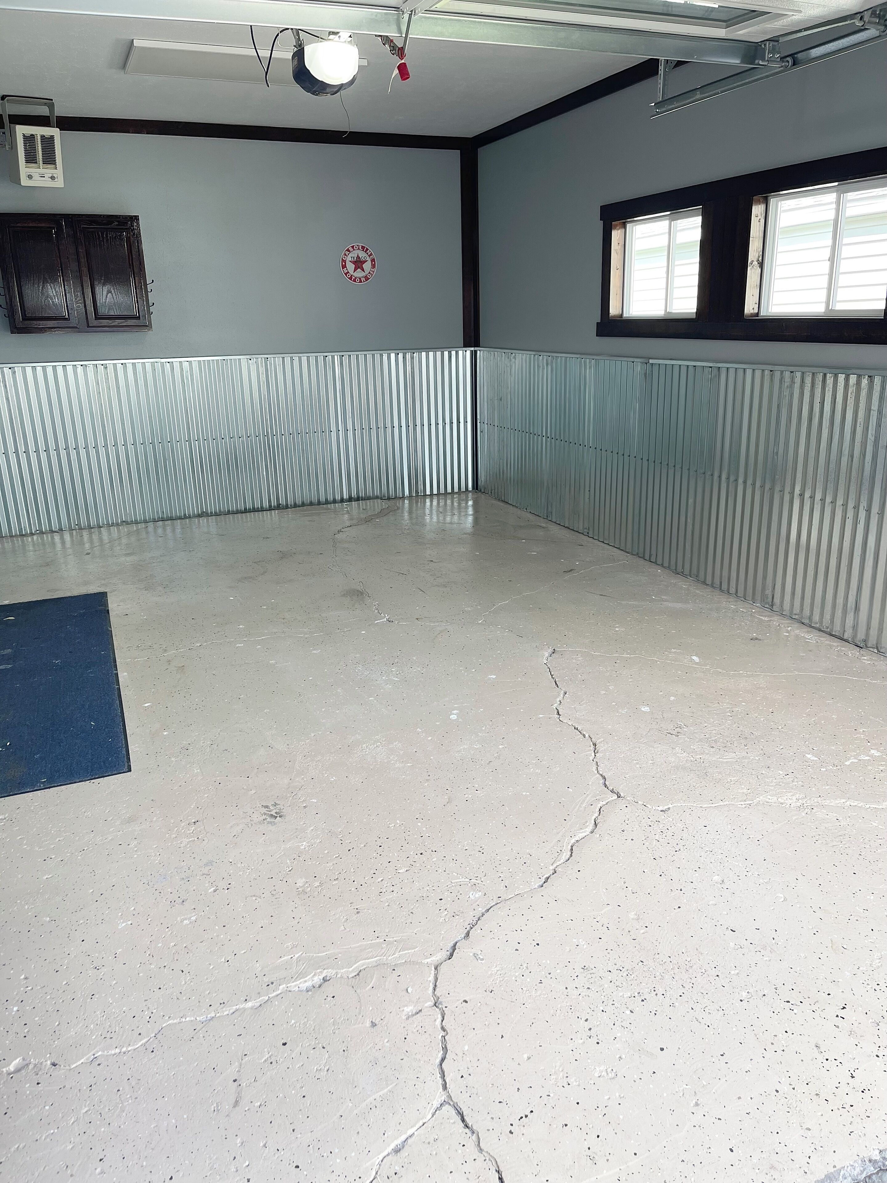 Una habitación amplia con suelo de hormigón, paredes de metal, una ventana y un ventilador de techo.