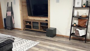 A living room with a wooden floor, a TV stand, a bookshelf, and a sofa. - Charming 3-bedroom house 3 mi to altru, 2 mi to UND, and 1 mi to down town (East Grand Forks)