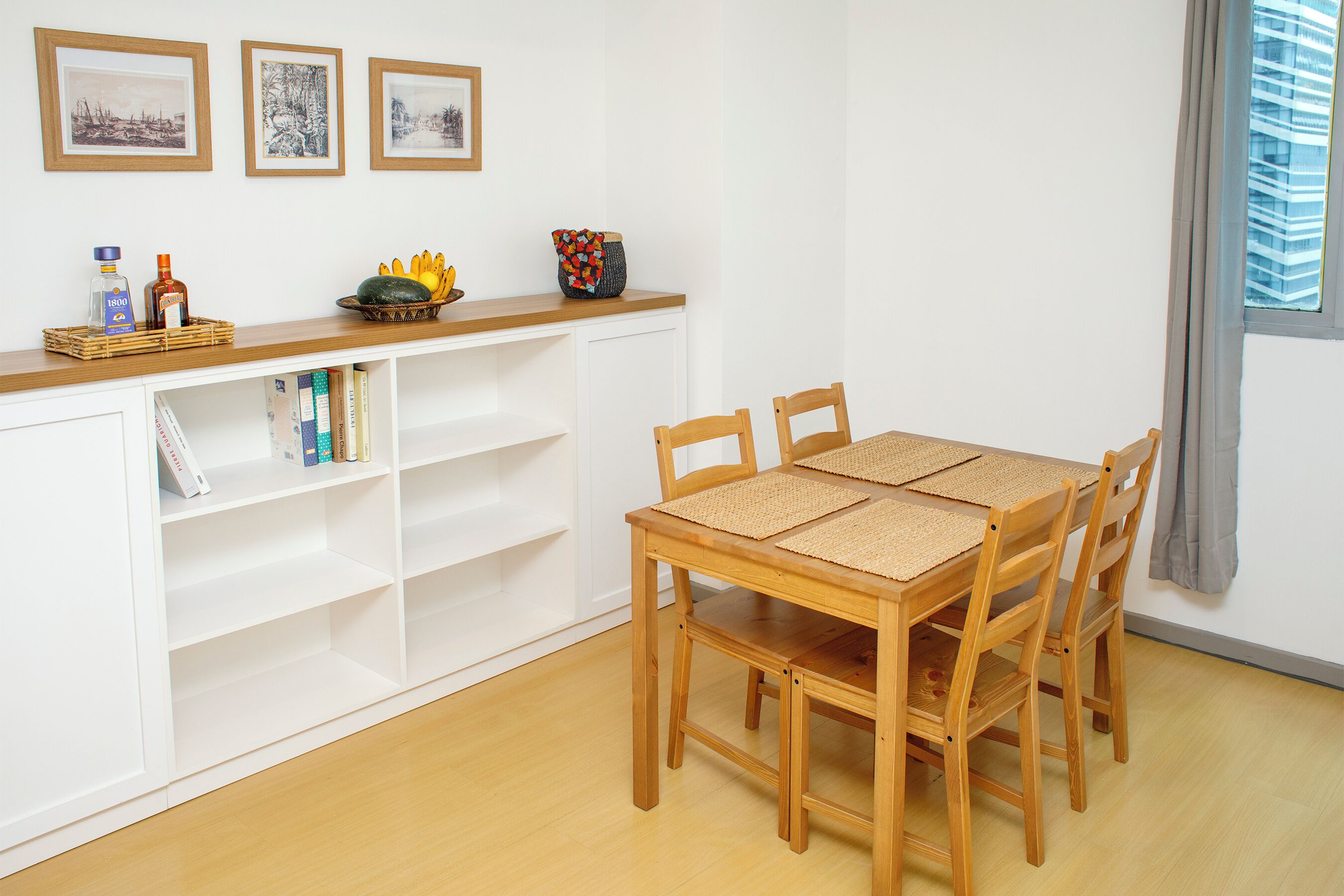 Un comedor con una mesa y sillas de madera, un armario blanco con estantes y una ventana con vistas a edificios.