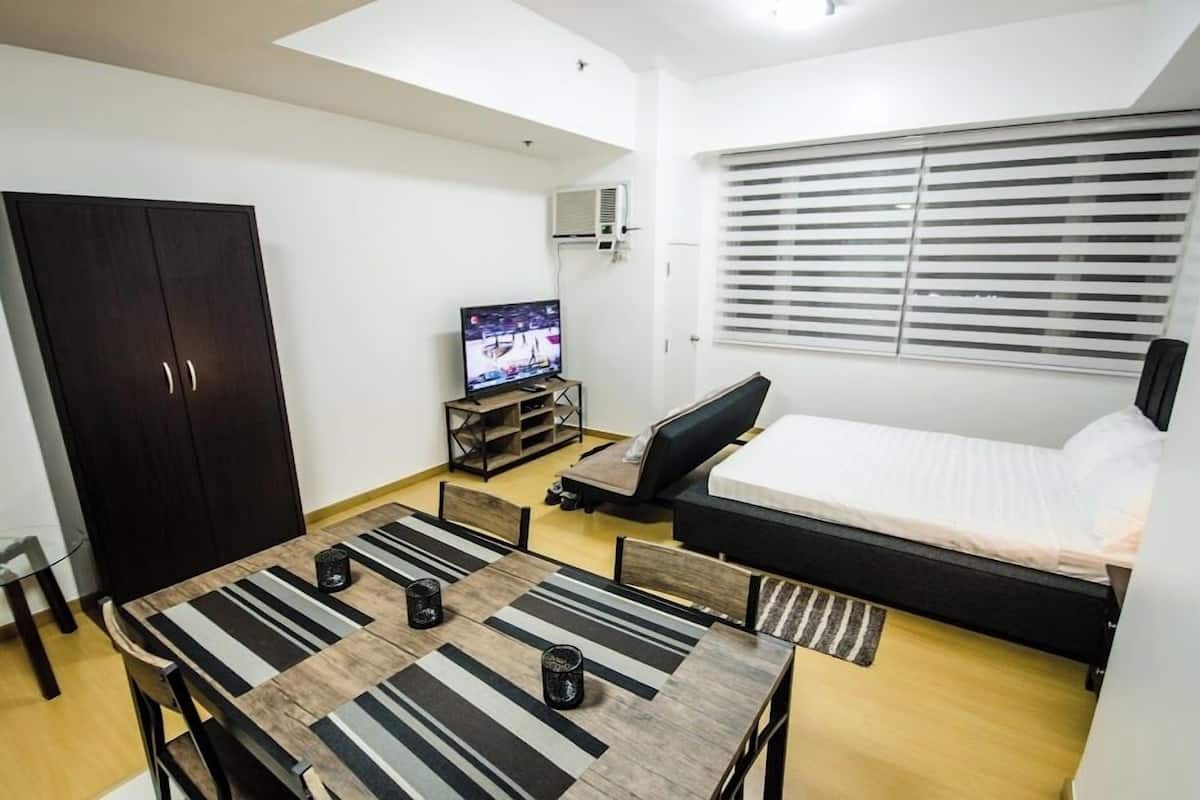A compact room with a bed, a TV, a dining table, and a wardrobe.