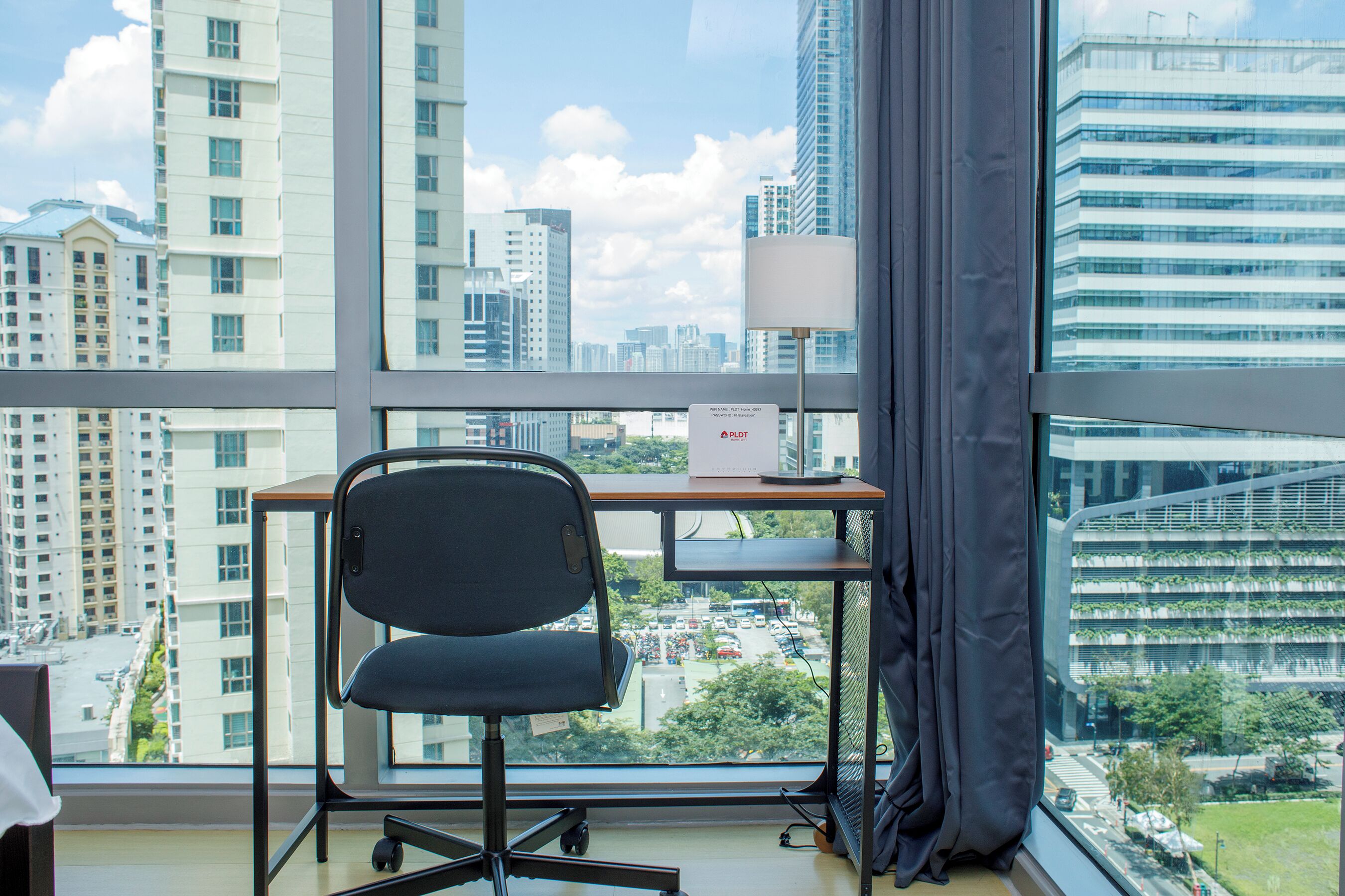 A modern office space with a large window, a desk, a chair, and a lamp.