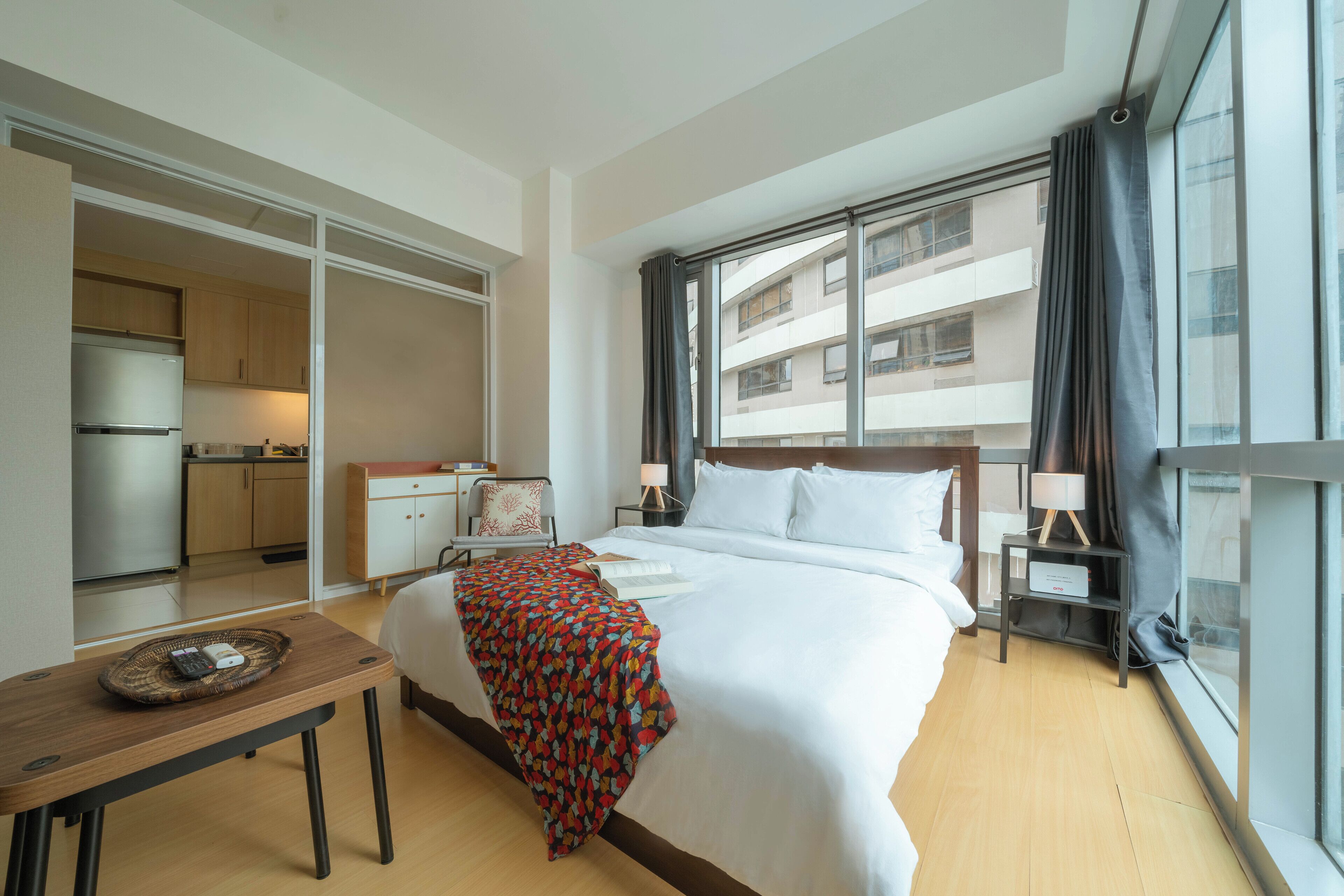 A hotel room with a bed, bedside table, lamp, and a view of the outside.