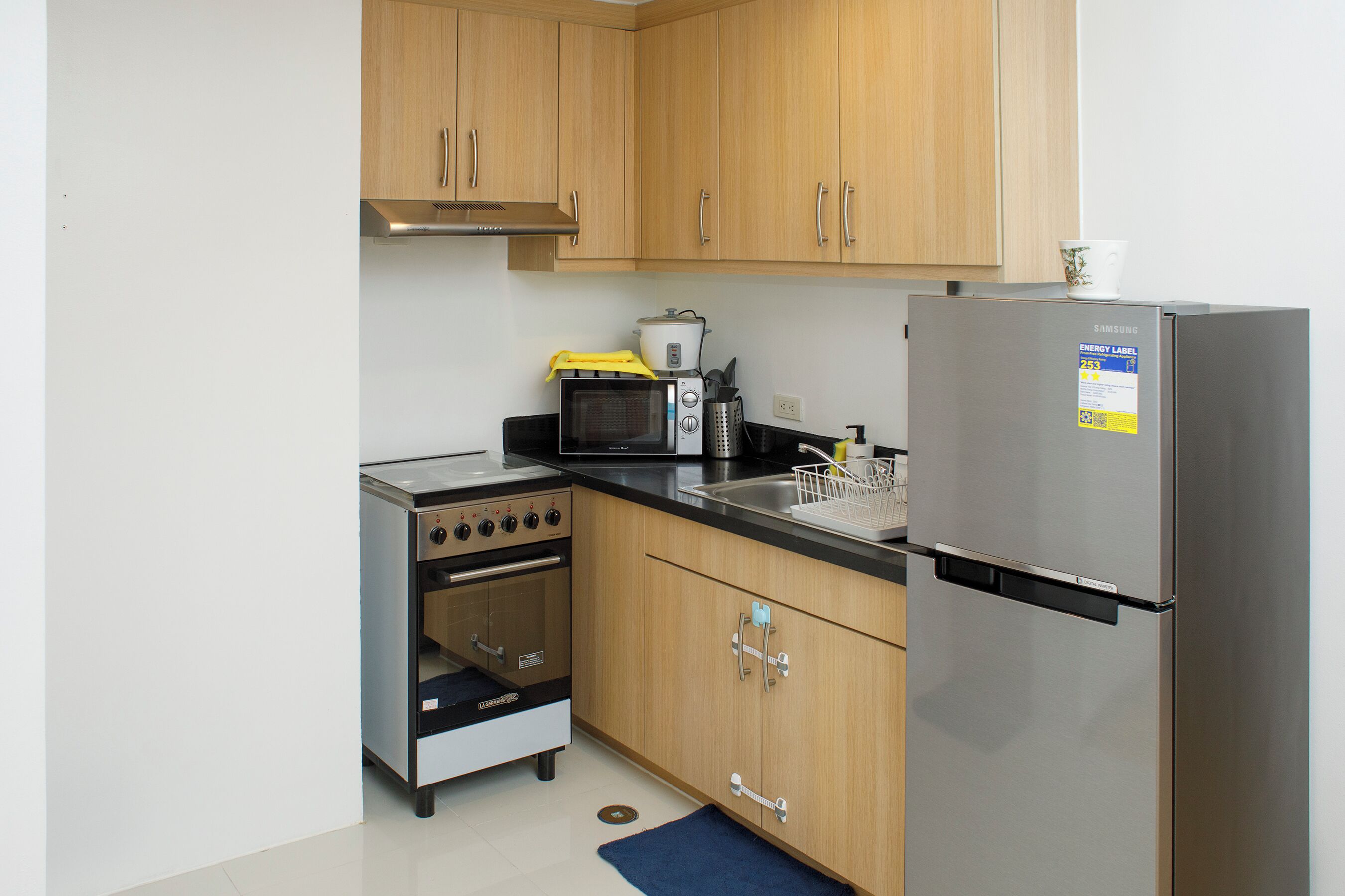 A compact kitchen with wooden cabinets, a stainless steel refrigerator, a microwave, a stove, and a sink.