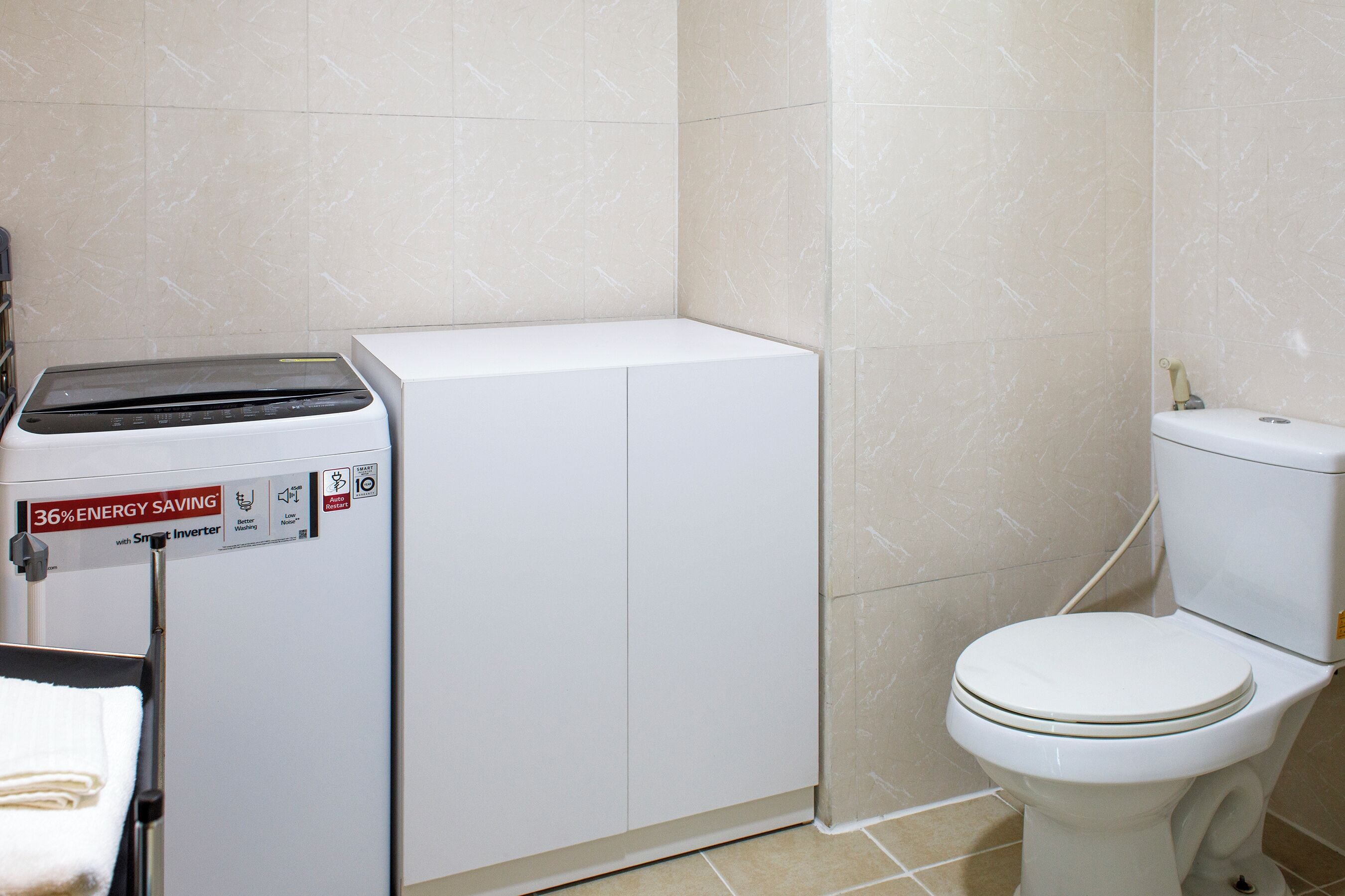 A compact bathroom with a white washing machine, a toilet, and a towel rack.