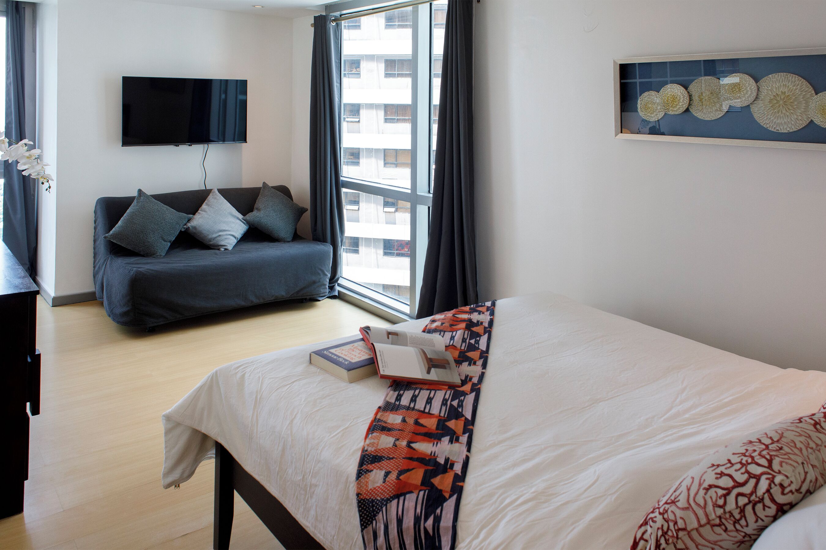 Habitación de hotel moderna con una cama grande, un sofá, un televisor de pantalla plana y una ventana con cortinas.