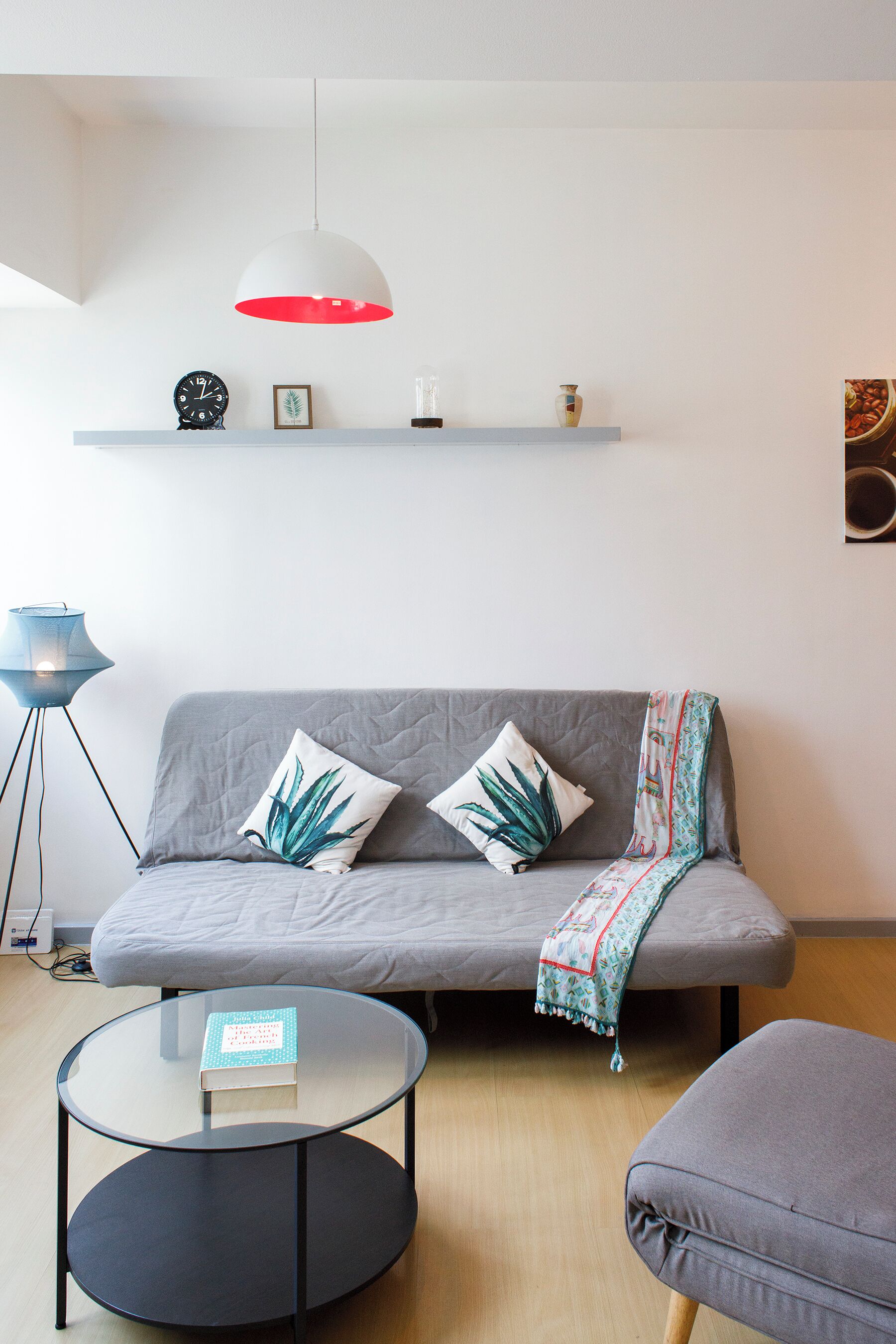Un salon moderne avec un canapé gris, une table basse ronde en verre, un lampadaire bleu et une suspension avec un abat-jour rouge.