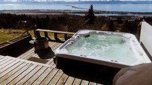 Un bain à remous sur une terrasse en bois, offrant une vue imprenable sur les montagnes et un lac.