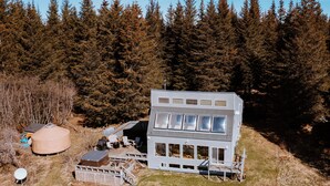 Une cabane moderne à deux étages, dotée de grandes fenêtres et entourée d’une forêt.