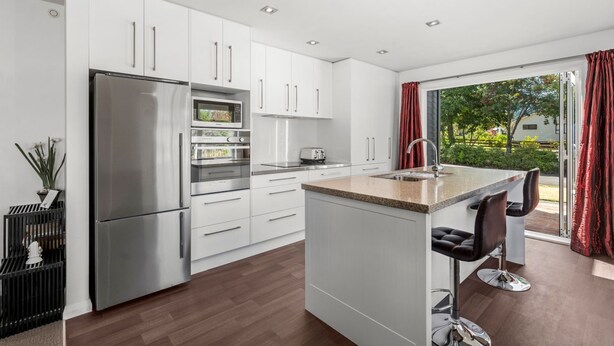 Una cocina moderna con armarios blancos, electrodomésticos de acero inoxidable y una isla grande con taburetes de bar.