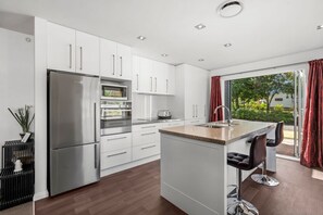 A modern kitchen with white cabinets, stainless steel appliances, and a large island with bar stools. - Kinloch Escape - 3 bedrooms, 3 Bathrooms (Taupo)