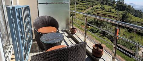 A balcony with wicker furniture and potted plants, overlooking a lush green landscape.