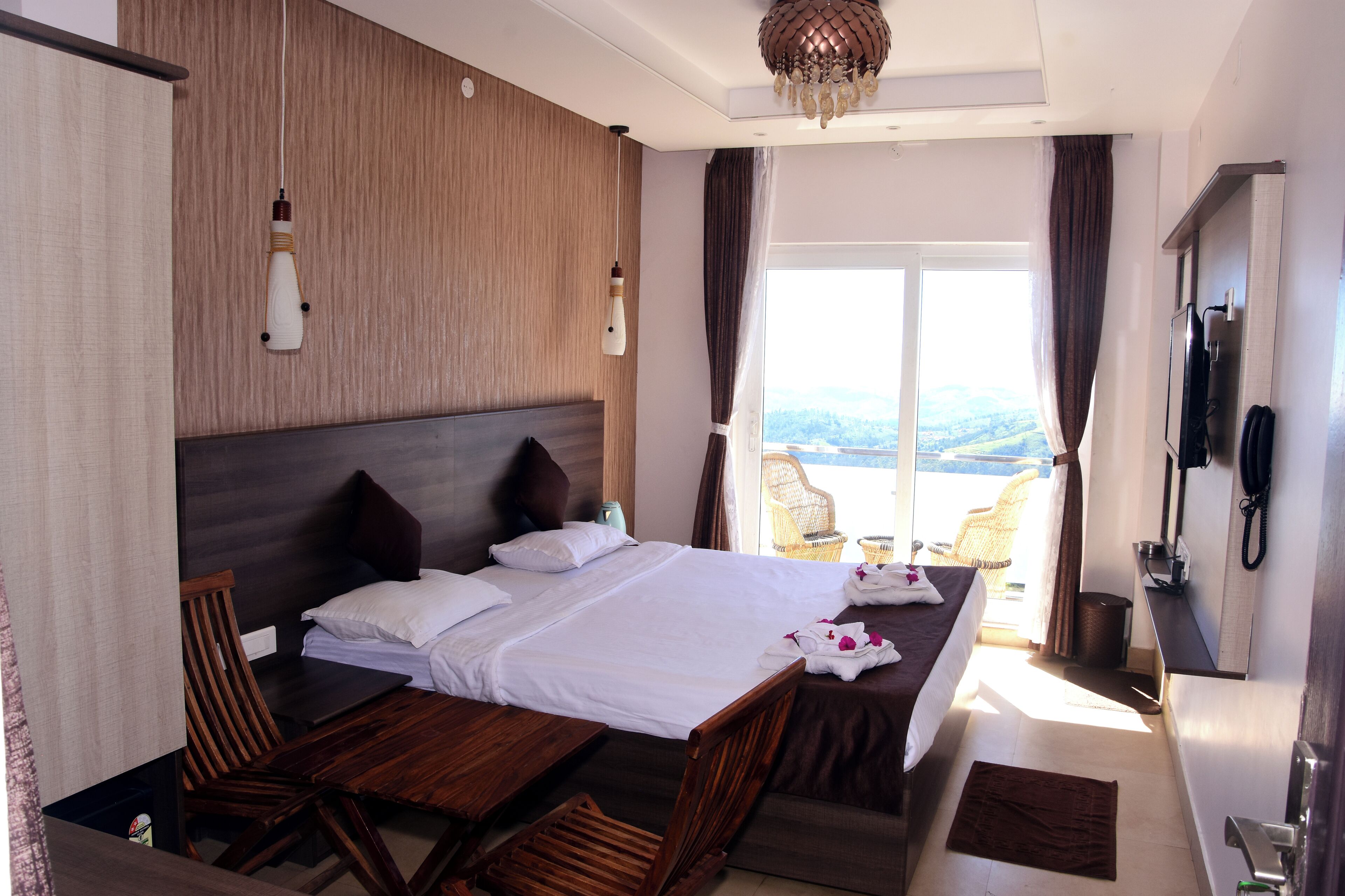 A hotel room with a large bed, wooden headboard, two bedside tables, a desk, a chair, and a view of the outdoors.