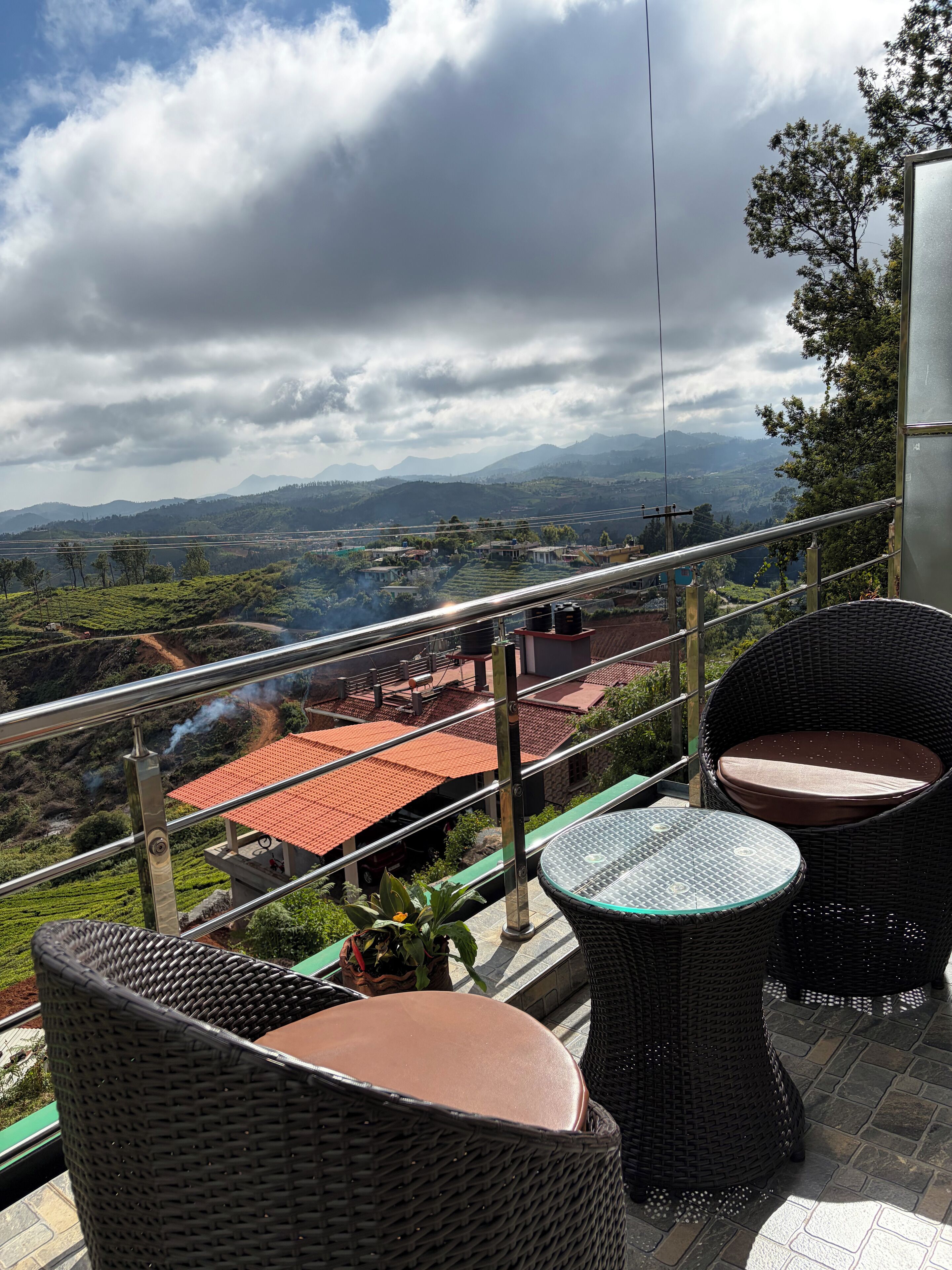 Una terrazza con sedie in vimini e un tavolo, con vista su un paesaggio pittoresco che include montagne e un fiume.