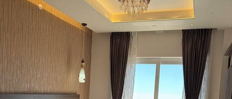 A modern hotel room with a large bed, a wooden headboard, a chandelier, and a view of the water.