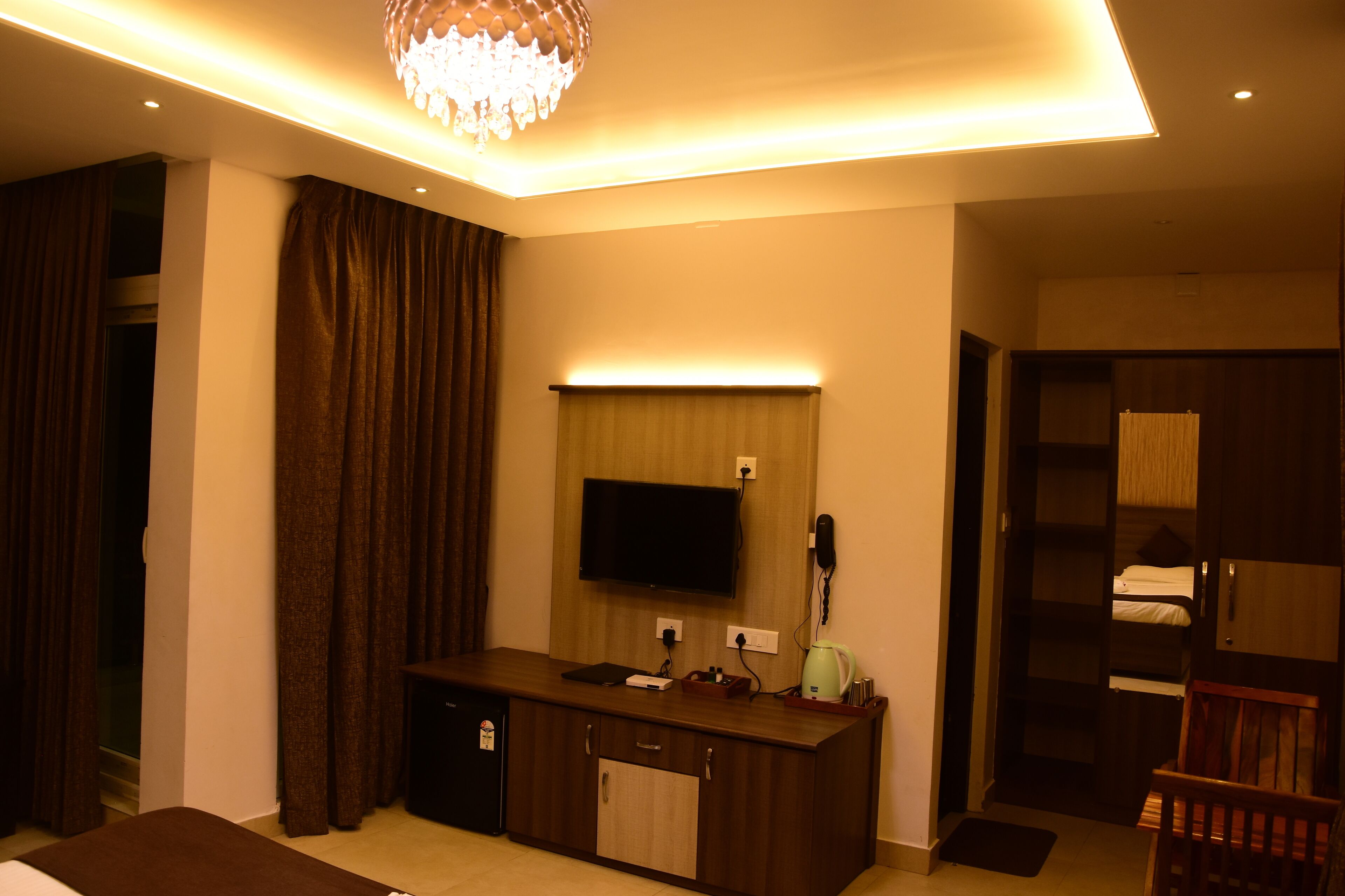 A hotel room with a wooden desk, a flat-screen TV, a minibar, and a wardrobe.