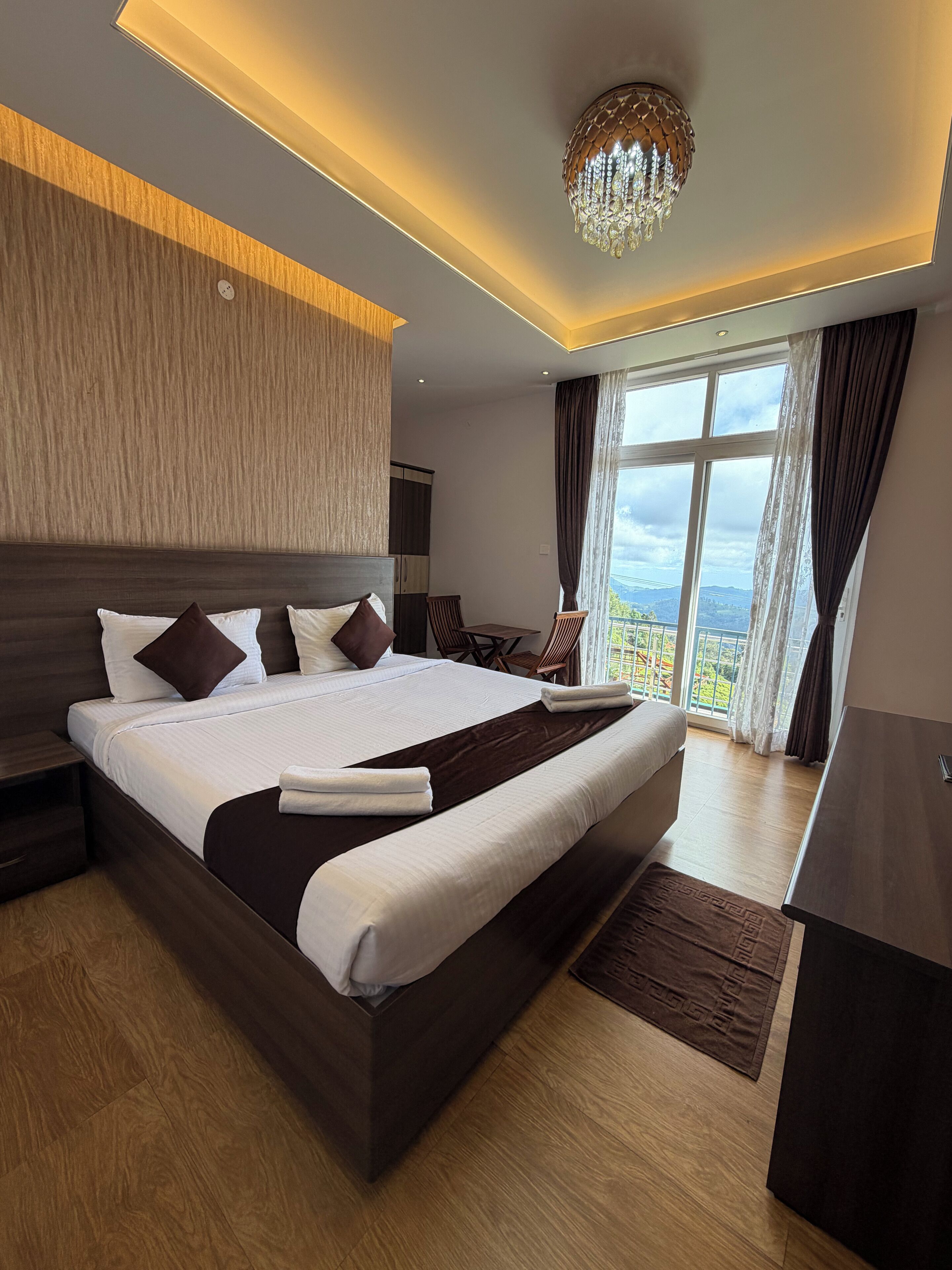 Una habitación de hotel moderna con una cama grande, una araña de cristal y vistas al exterior.
