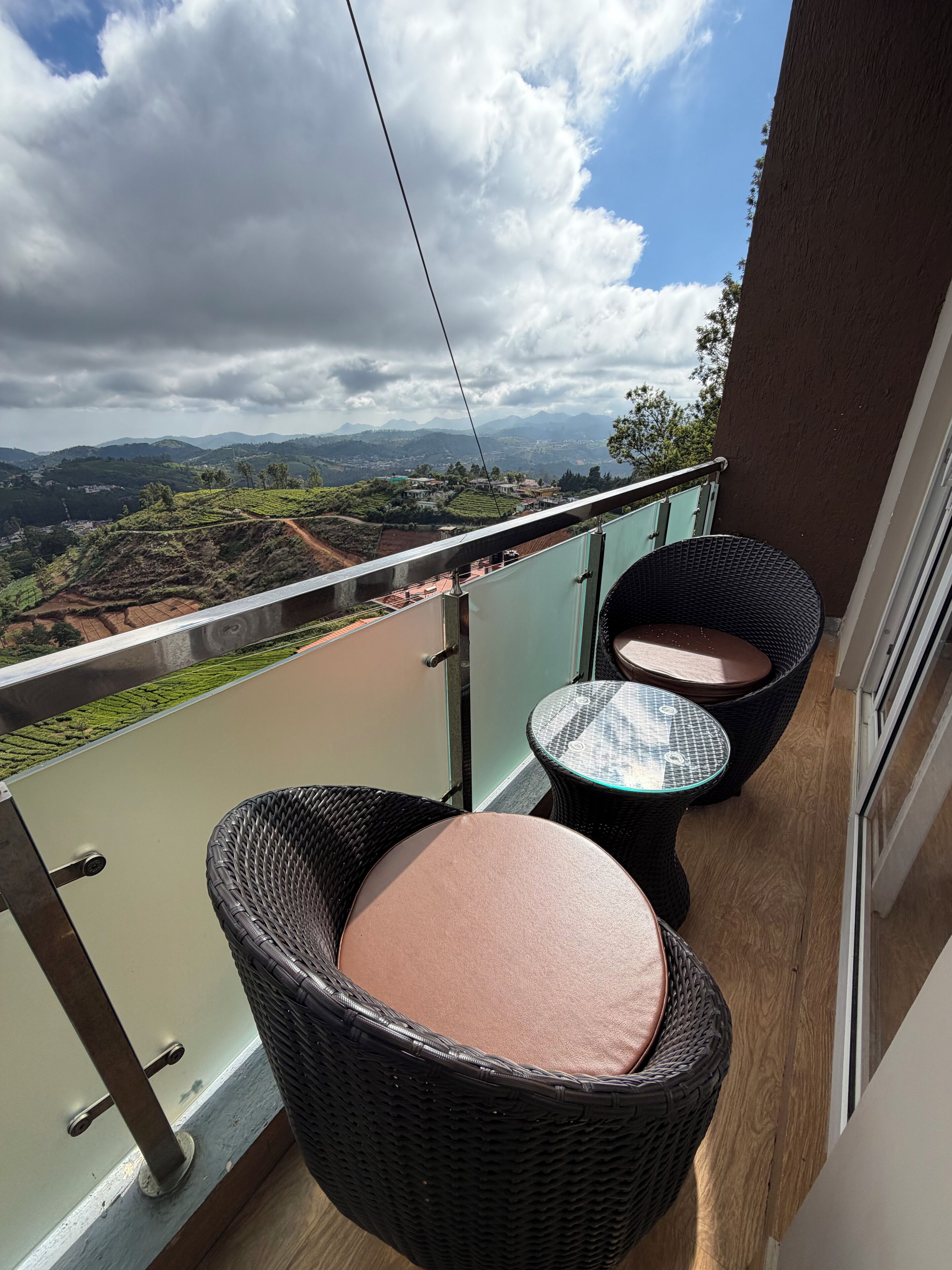 A balcony with wicker chairs and a glass railing overlooking a scenic landscape.