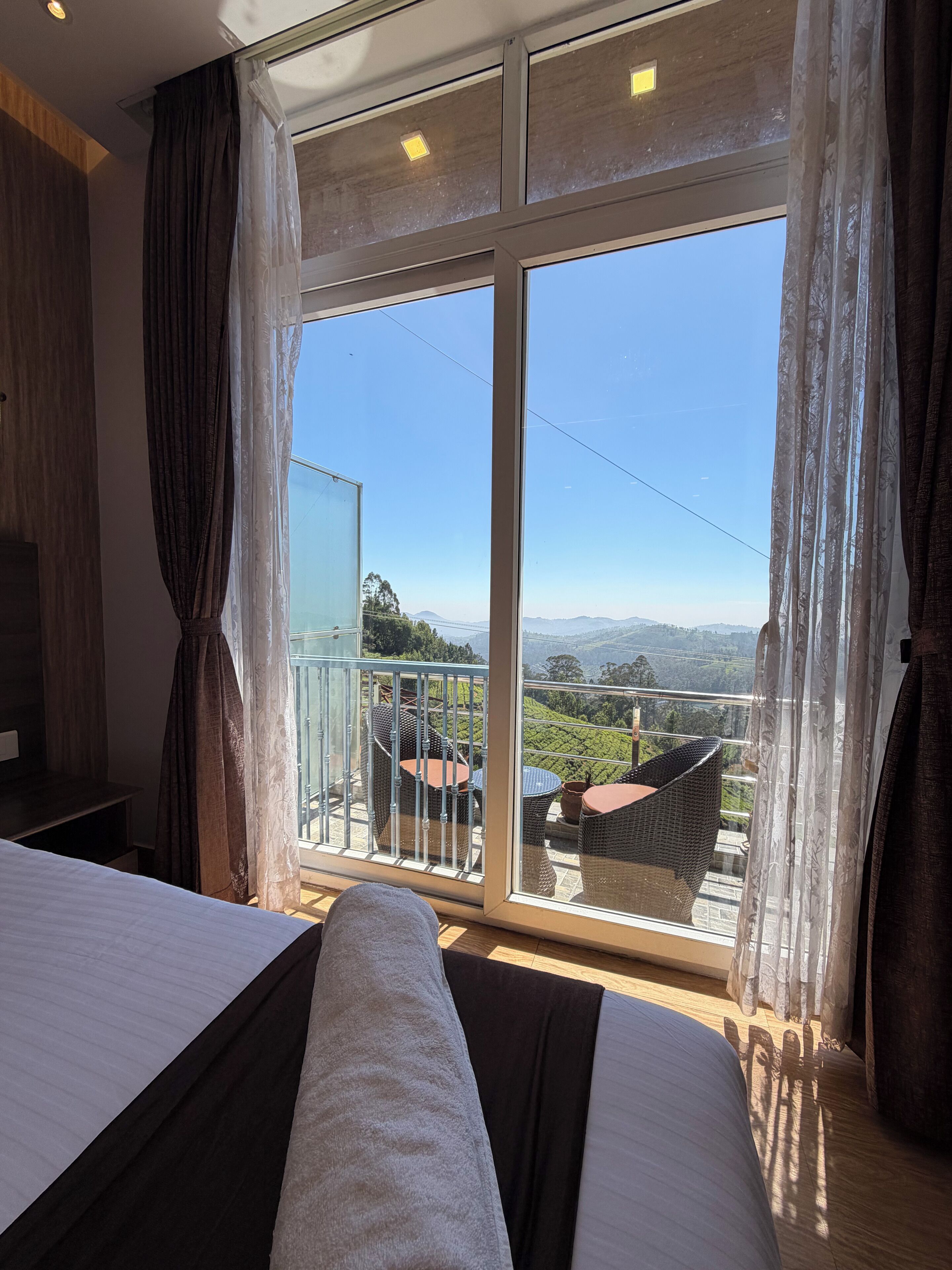 A hotel room with a large balcony, a bed, and a view of the landscape.