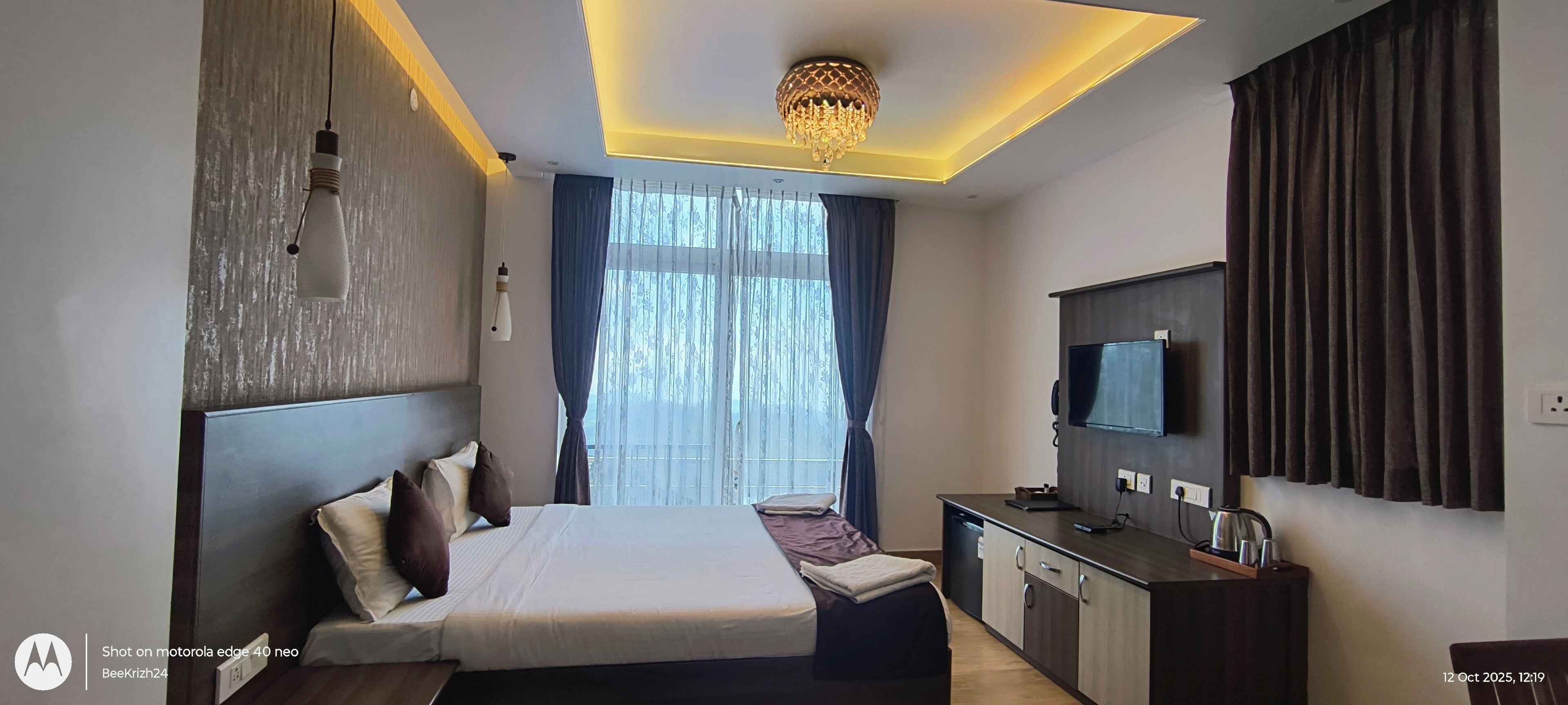 Een moderne hotelkamer met een groot bed, een bureau, een televisie en een kroonluchter.