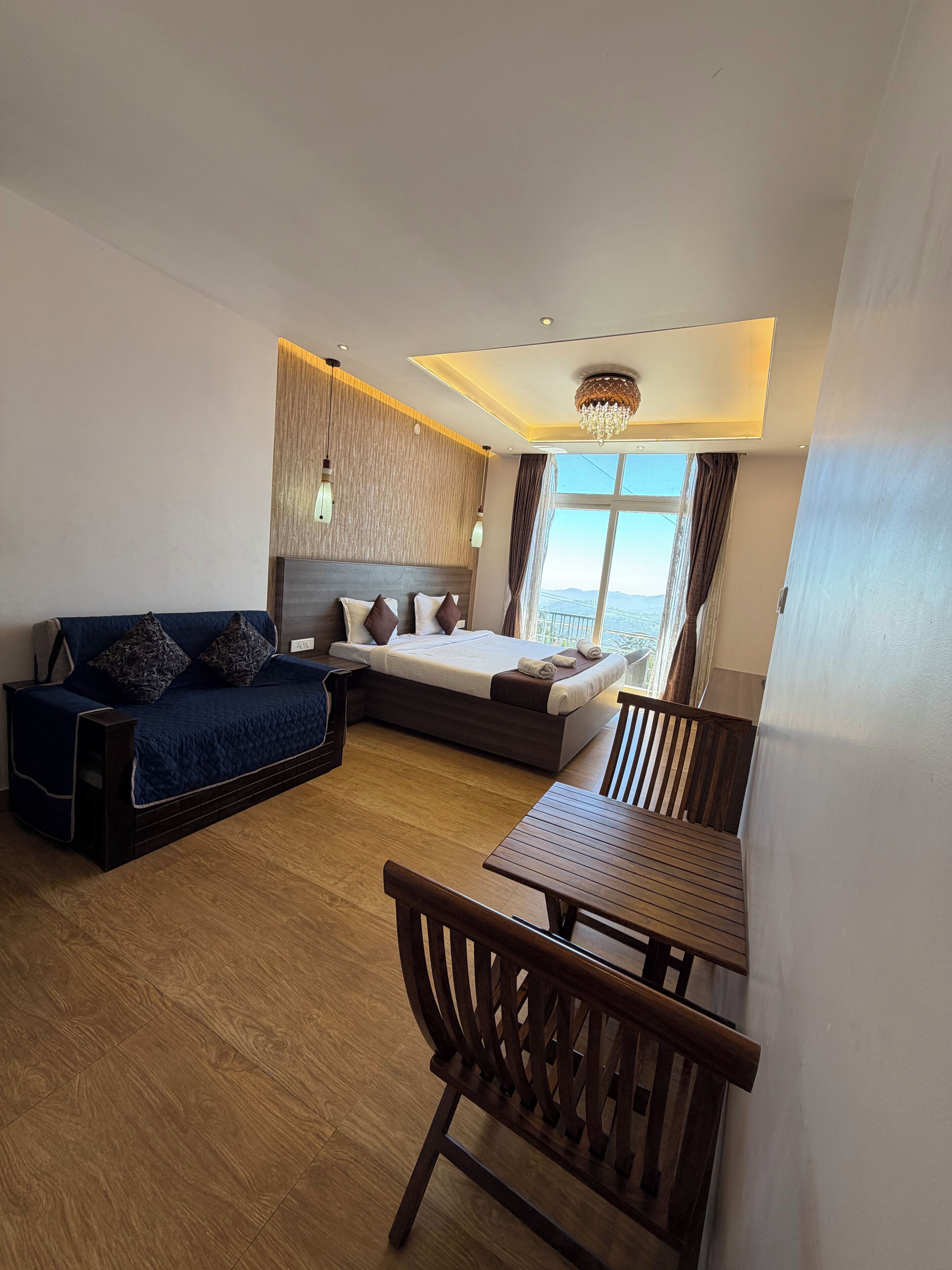 Een moderne hotelkamer met een bed, een bank, een eettafel en uitzicht op de omgeving.