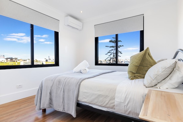 Un dormitorio moderno con cama, ventanas amplias y vista a un paisaje urbano.